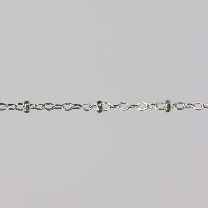 Close-up of a silver chain with beads on a light gray background