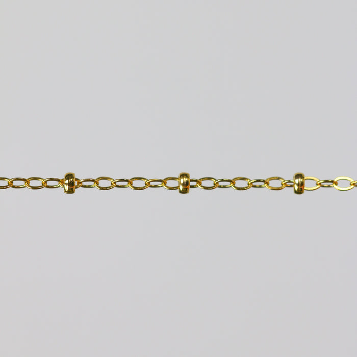Gold chain with small cylinder beads on a light gray background