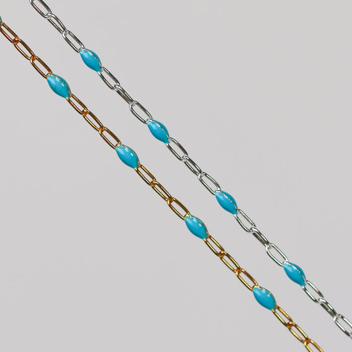 A yellow gold and a sterling silver chain with turquoise light blue enamel over a gray background