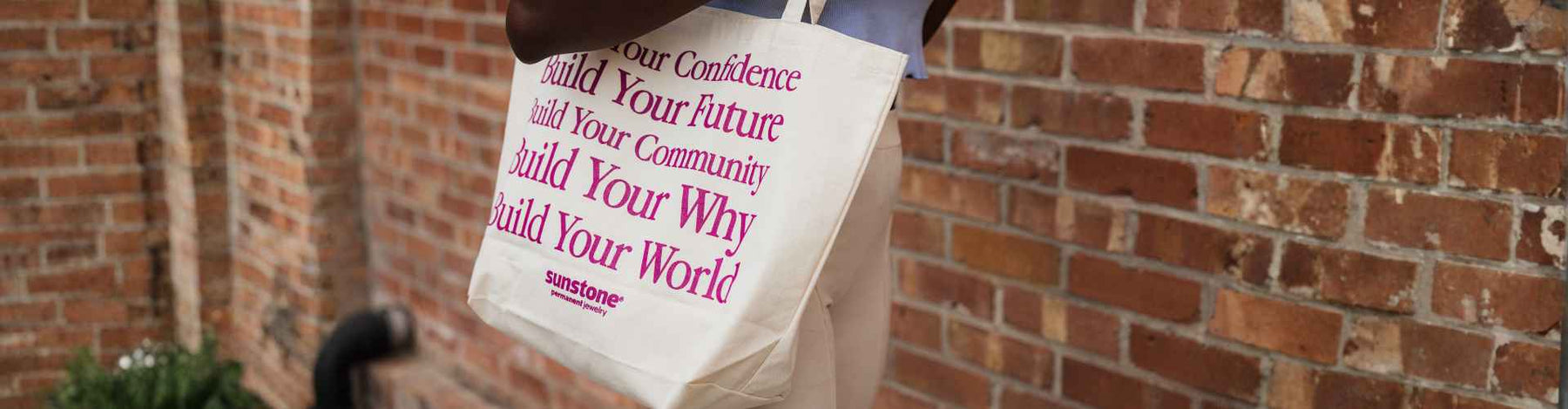 A woman walking to  her next permanent jewelry event wearing a Sunstone Permanent Jewelry tote bag