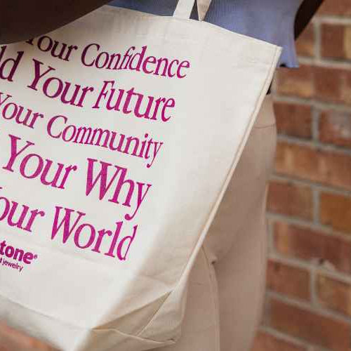A woman walking to  her next permanent jewelry event wearing a Sunstone Permanent Jewelry tote bag