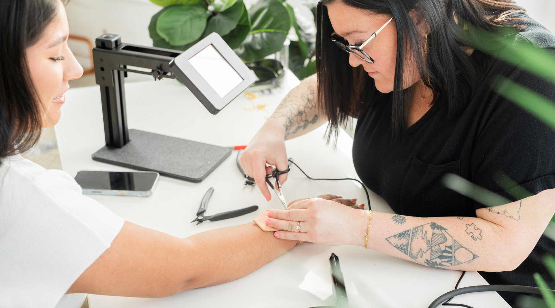 a woman running a permanent jewelry business is welding a permanent jewelry bracelet onto a female customer using a sunstone welding machine