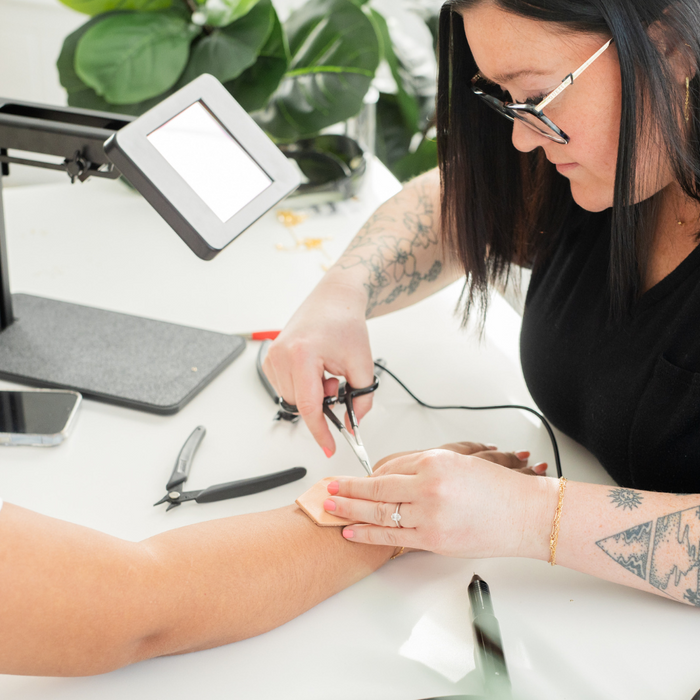 a woman running a permanent jewelry business is welding a permanent jewelry bracelet onto a female customer using a sunstone welding machine