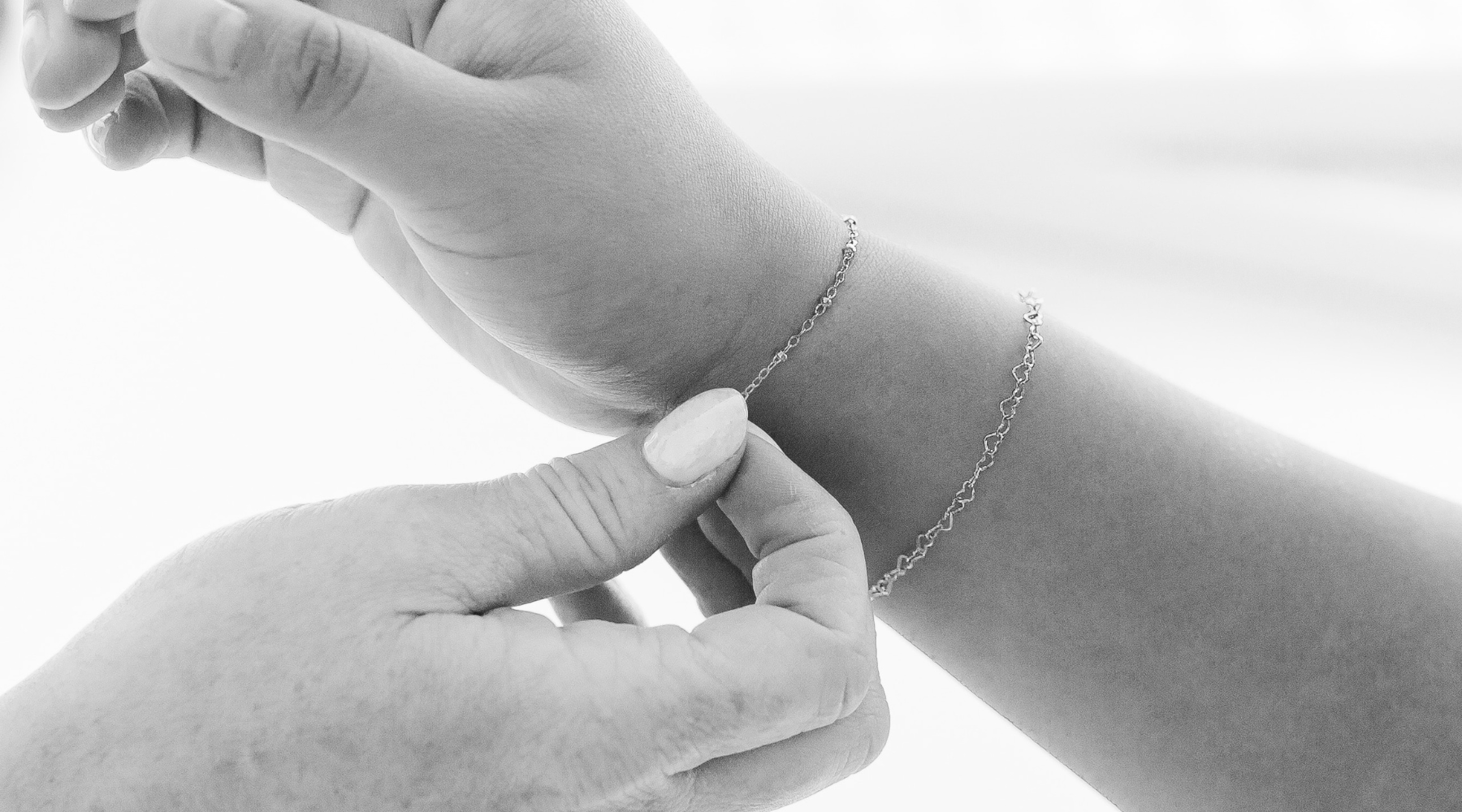 a black and white photo of someone adjusting the chain on their wrist for a permanent jewelry bracelet