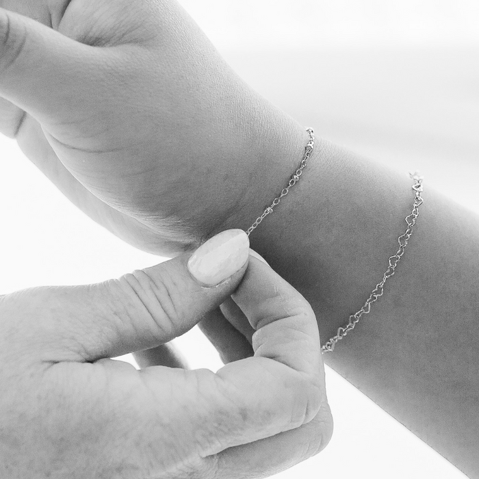 a black and white photo of someone adjusting the chain on their wrist for a permanent jewelry bracelet