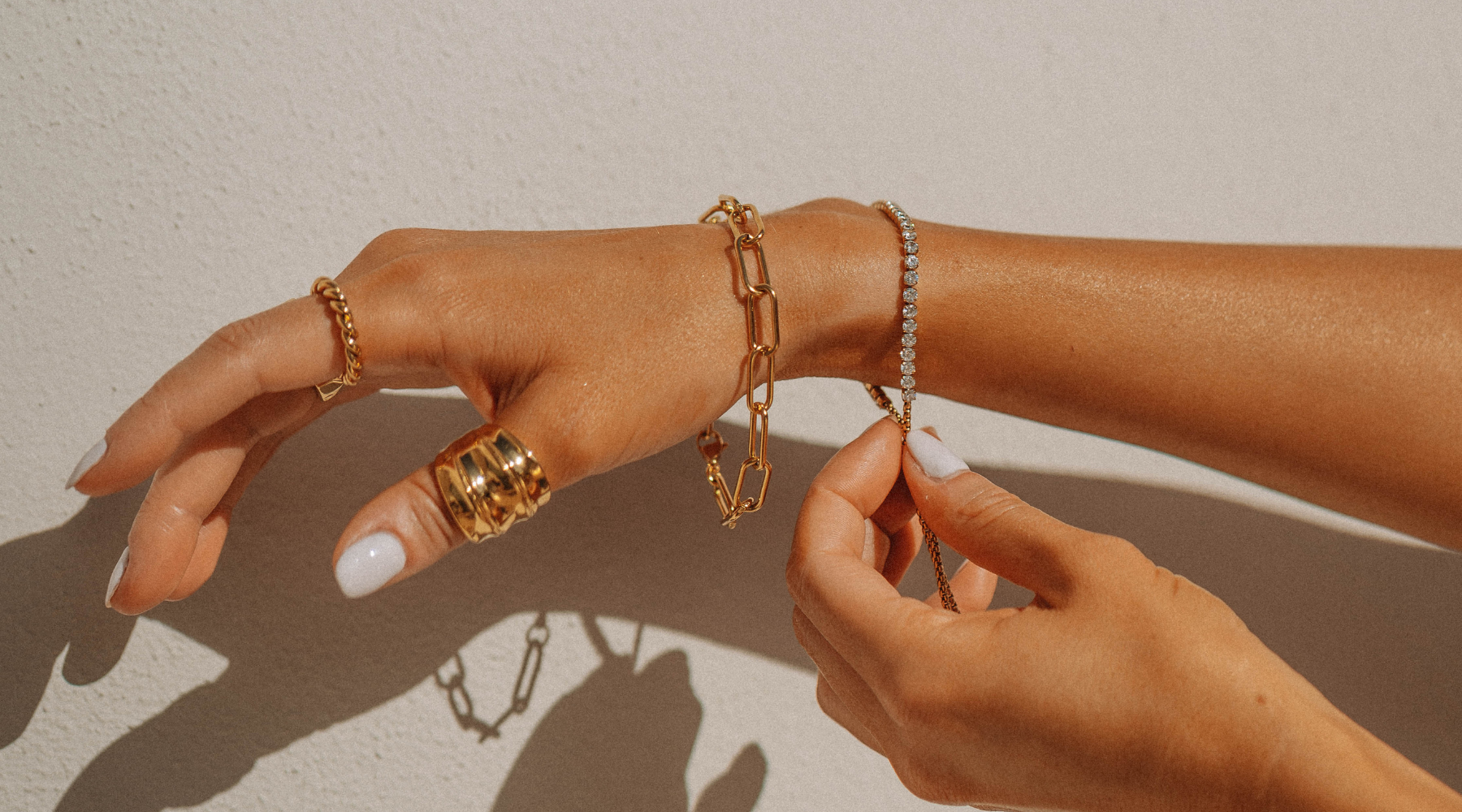 Half of an arm with gold rings and gold permanent jewelry bracelets. It's a warm image to show the colors of gold-plated jewelry.