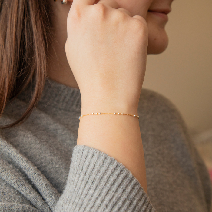 Person wearing a gold mixed metal silver beaded pj chain bracelet on a blurred background