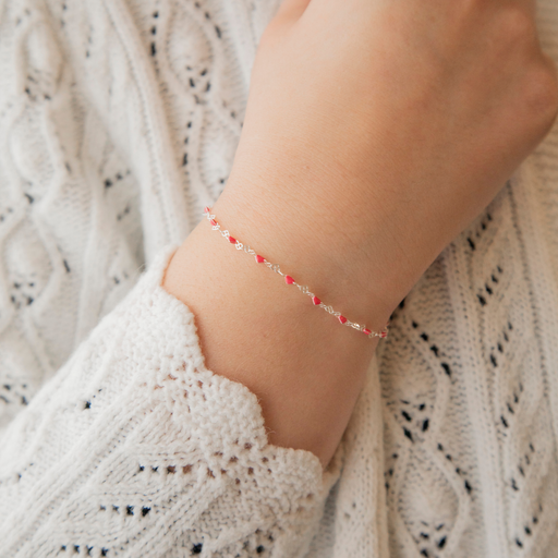 Close-up of a wrist wearing a delicate heart link bracelet with enamel and a textured sweater background