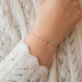 Close-up of a wrist wearing a delicate heart link bracelet with enamel and a textured sweater background
