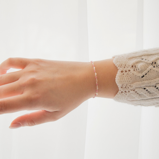 Hand wearing a delicate heart link bracelet chain with pink rose enamel on a plain background