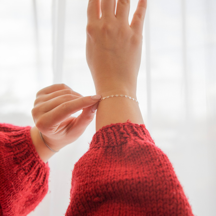 Person wearing a red sweater with a permanent jewelry bracelet on a white background. The bracelet chain is a figaro and starburst design.