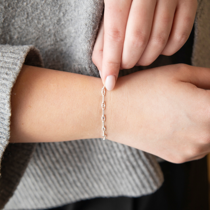 Person wearing a silver pj chain bracelet with a cz gemstone on a neutral background
