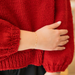 Close-up of a hand wearing a gold infinity link bracelet chain on a red knitted sleeve.
