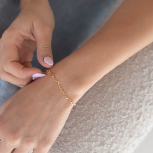 Person wearing a gold clover pj chain on their wrist sitting on a chair.