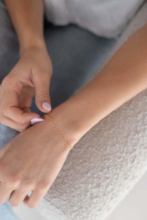 Person wearing a gold clover pj chain on their wrist sitting on a chair.