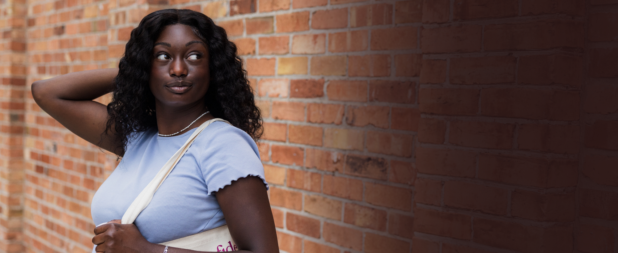 Woman standing against a brick wall wearing a light blue top.