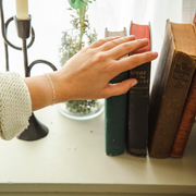 Hand reaching for a book on a shelf with the silver Leah chain on the wrist of said hand.