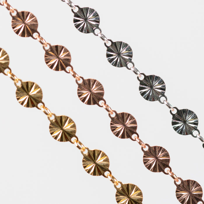 Close-up of a permanent jewelry chain with circular metal pendants with a hammered starburst design on a light gray background