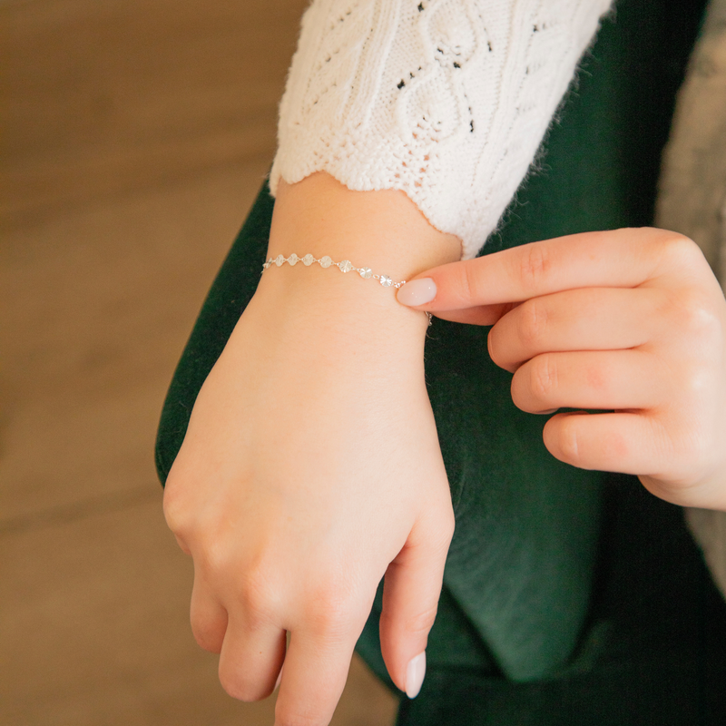 Person wearing a starburst disk permanent jewelry bracelet chain on a blurred background