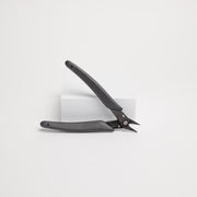 Black pliers leaning on a white box against a white background