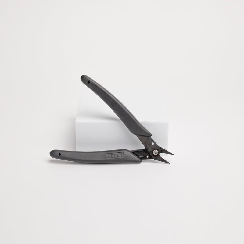 Black pliers leaning on a white box against a white background