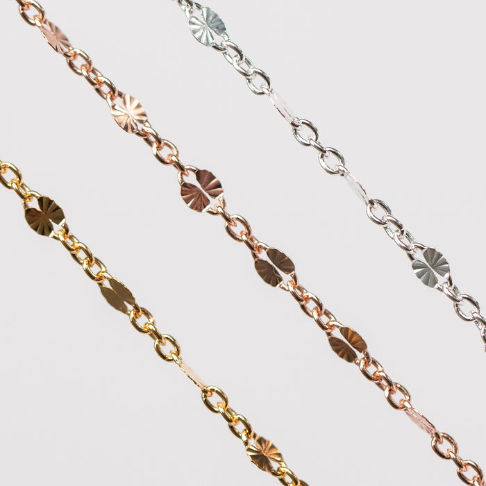 Two gold filled figaro permanent jewelry and one silver chain with a hammered starburst design on a light gray background