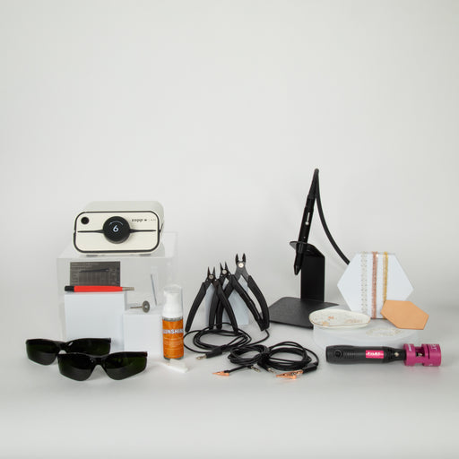 Collection of permanent jewelry tools, chain, accessories, and welding equipment on a white surface with a white background