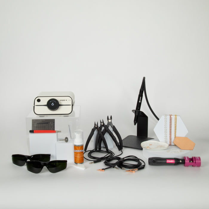 Collection of permanent jewelry tools, chain, accessories, and welding equipment on a white surface with a white background