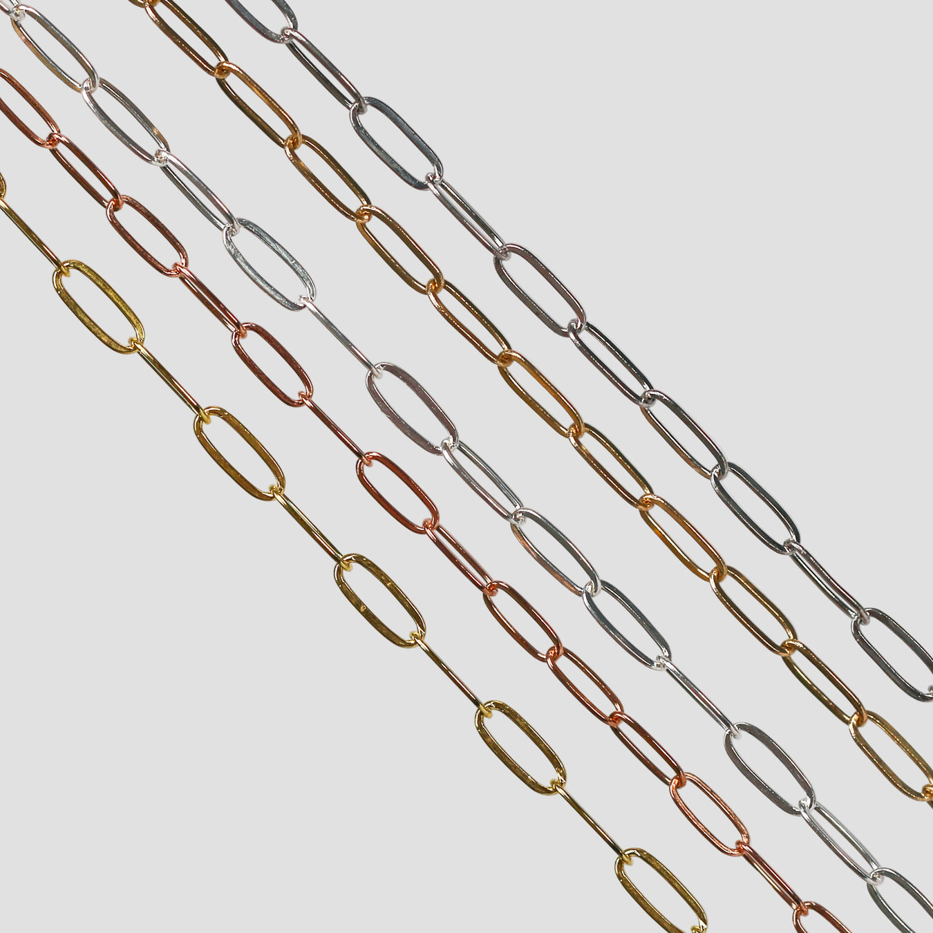 Flat elongated oval chains laid out side by side in different metal types. 14 karat gold, 14/20 gold filled, and sterling silver options are depicted.
