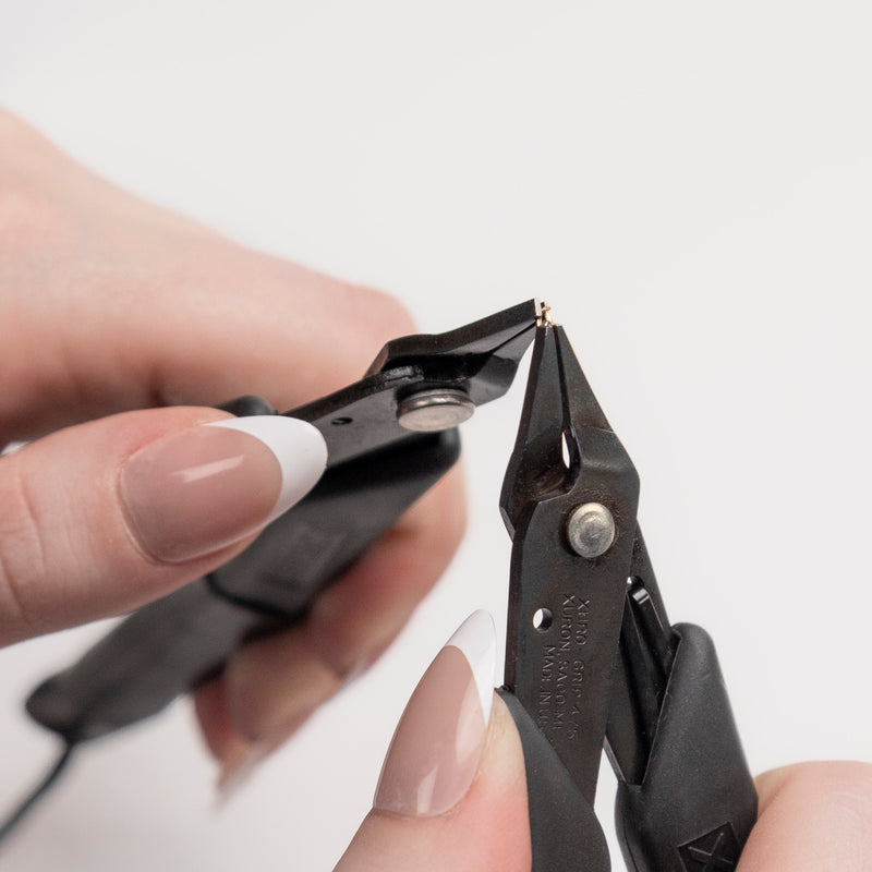 Close-up of hands using a pair of black pliers on a white background