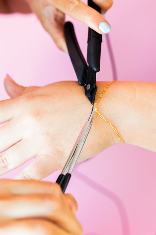 Gold permanent jewelry chain being welded onto a customers wrist with a pink background