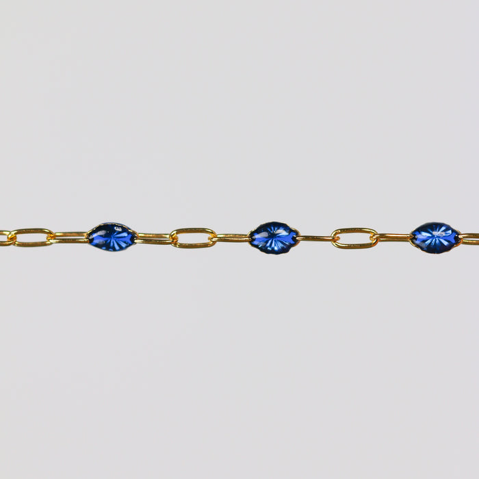 Gold permanent jewelry chain bracelet with sparkly blue enamel on a light gray background