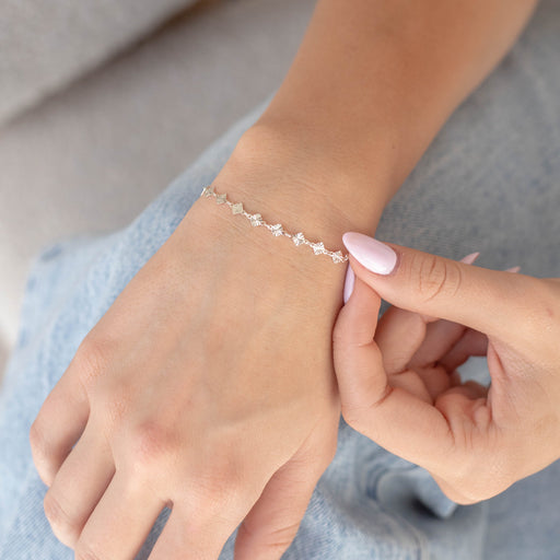Woman sitting with a silver diamond shape disk permanent jewelry chain on her wrist.