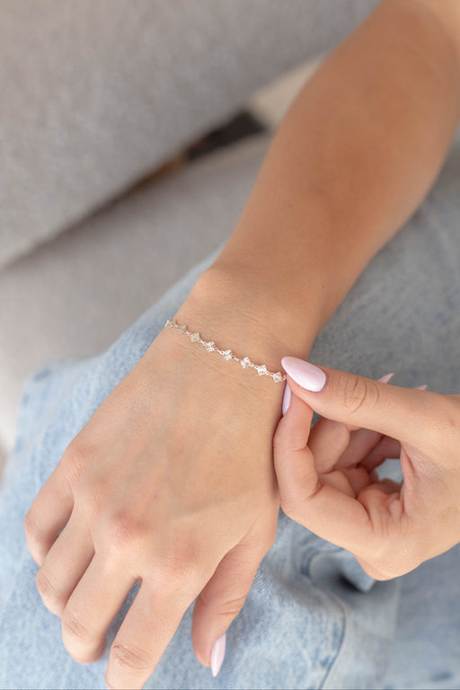 Woman sitting with a silver diamond shape disk permanent jewelry chain on her wrist.