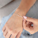 Woman sitting with a silver diamond shape disk permanent jewelry chain on her wrist.