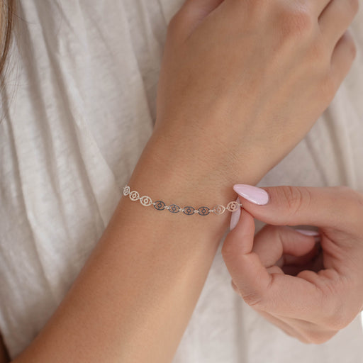 Person adjusting a silver bracelet chain on their wrist against a neutral background