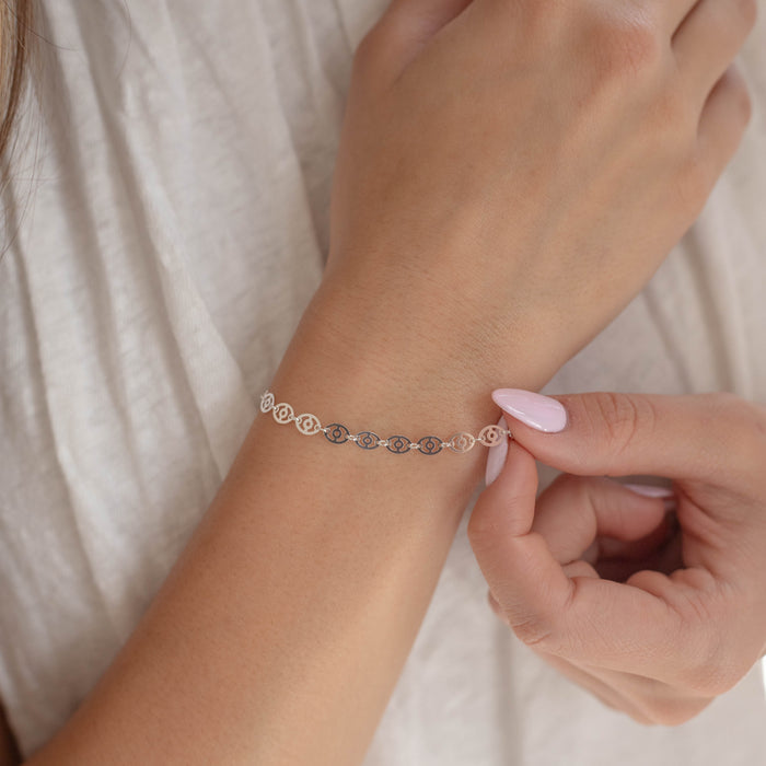 Person adjusting a silver bracelet chain on their wrist against a neutral background