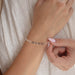 Person adjusting a silver bracelet chain on their wrist against a neutral background