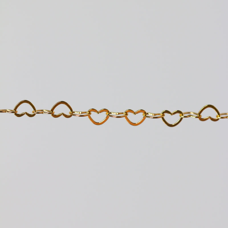Yellow gold chain with heart-shaped links on a light gray background