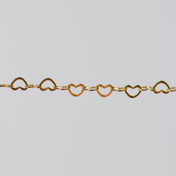 Yellow gold chain with heart-shaped links on a light gray background