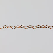 Rose gold chain with flat heart shaped links on a gray background