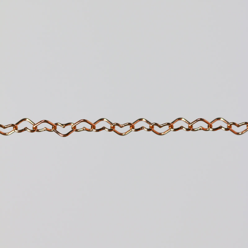 Rose gold chain with flat heart shaped links on a gray background