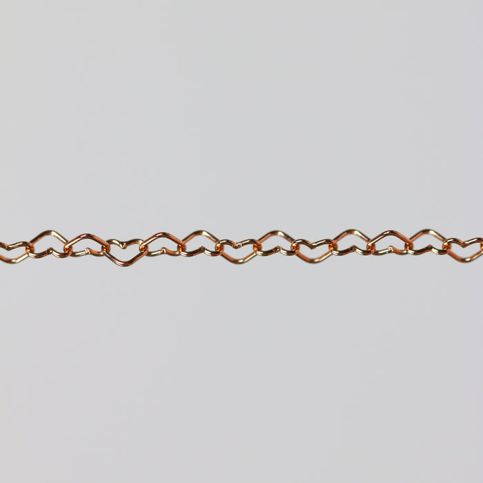 Rose gold chain with flat heart shaped links on a gray background