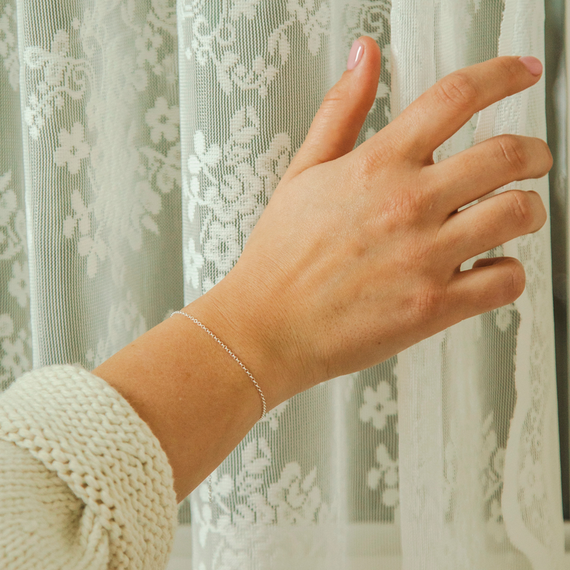 Hand with a silver bracelet with Rolo Links in a Belcher Design in front of a lace curtain