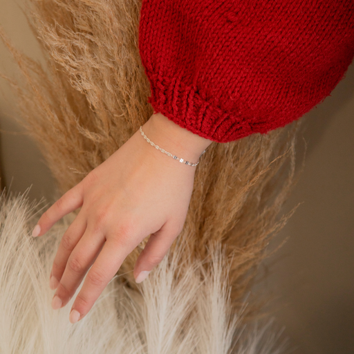 Hand wearing a silver textured pj chain on a neutral background.