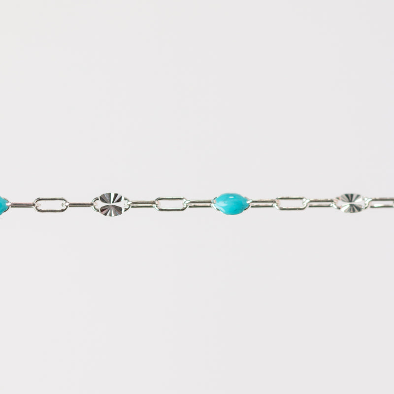 Silver chain bracelet with turquoise beads made from enamel on a light gray background