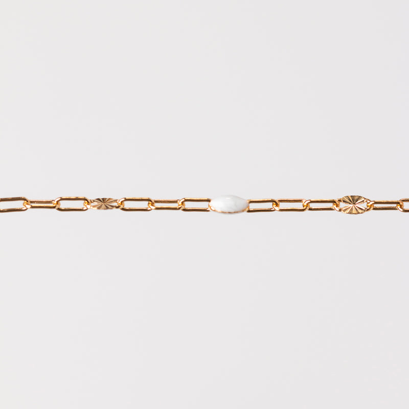 Yellow gold chain bracelet with a white enamel on a light gray background
