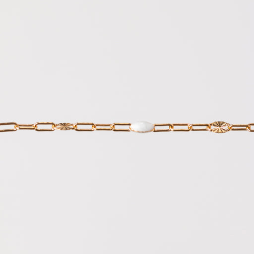 Yellow gold chain bracelet with a white enamel on a light gray background