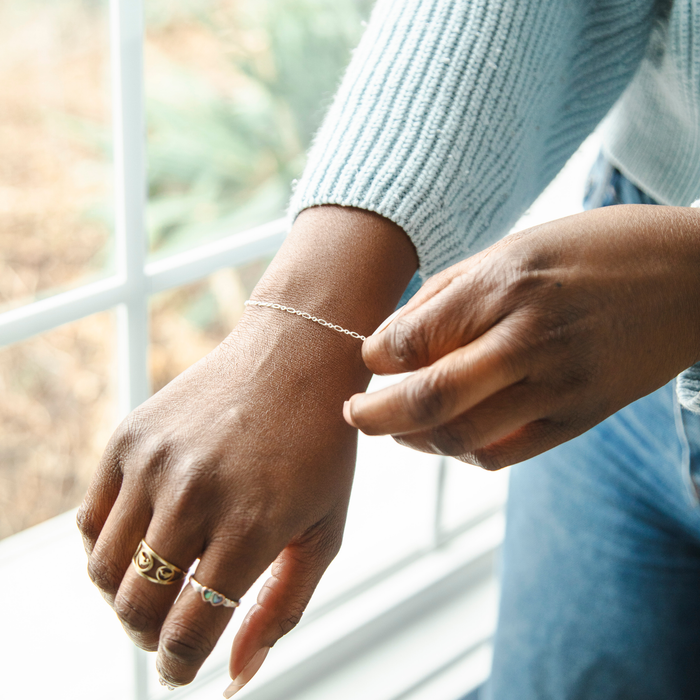 Woman wearing a silver bracelet on her wrist with a blurred outdoor background behind the woman