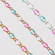 Up close of three chains with links that are gold, rose gold, and silver. Enamel beads in pink, blue, and white are shown.